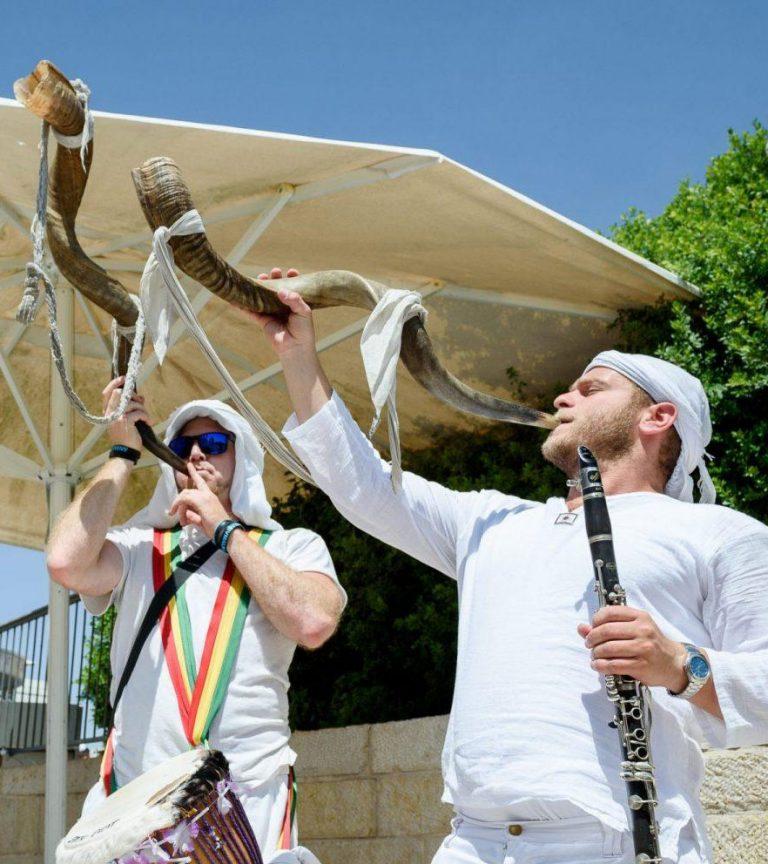 Two street musicians in Israel playing horns and holding other instruments.