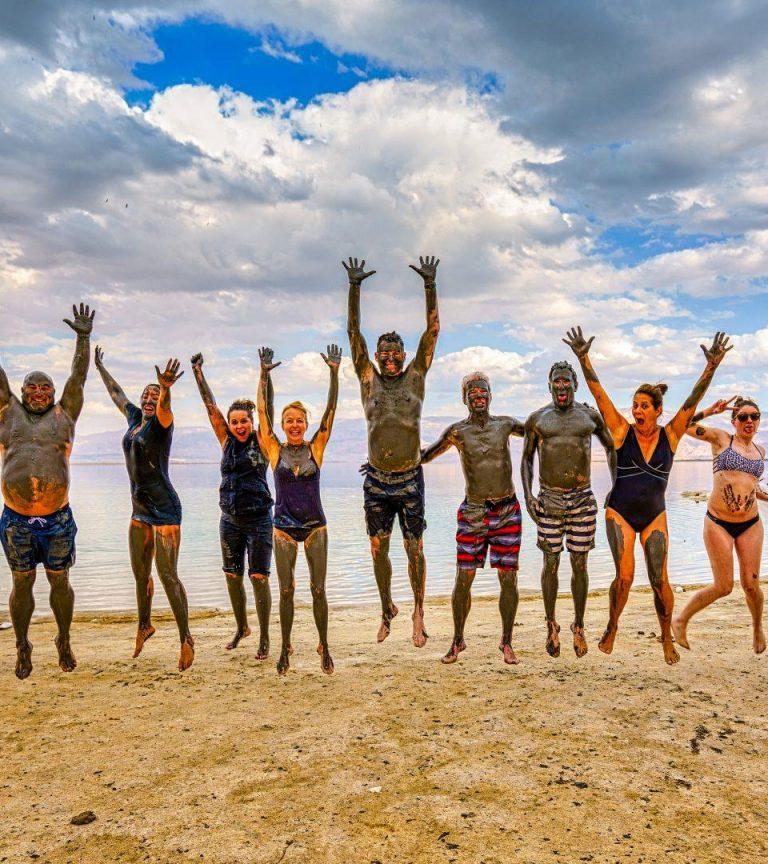 Muddy travelers jumping for joy at the dead sea in Israel