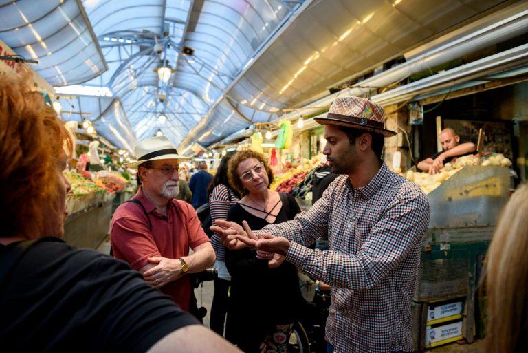 A Via Sabra tour guide talking to a group of tourists in a market in Israel.