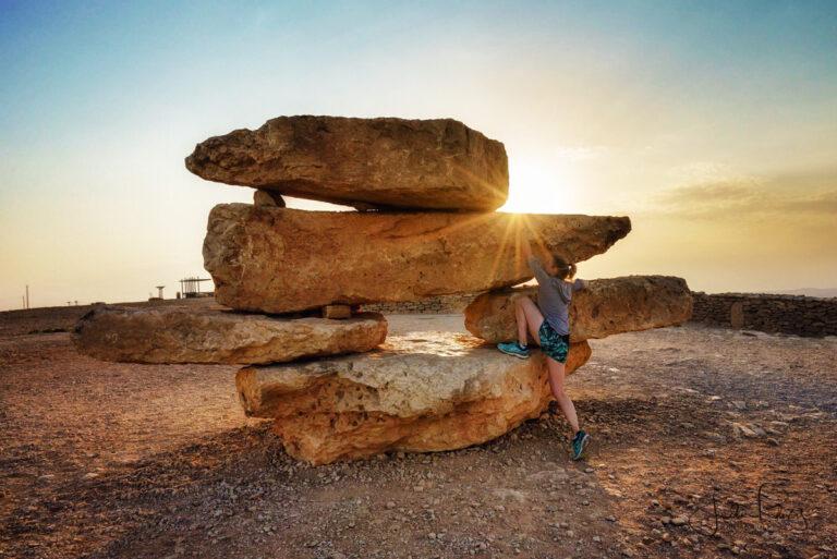 A Via Sabra guest climbing a stack of large boulders in the desert.