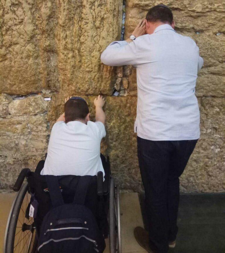 A man and a boy in a wheelchair praying at the Western Wall in Jerusalem.