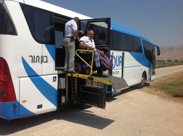 A bus driver lowering a male passenger in a wheelchair from his bus using a mobility lift during a holy land tour for the disabled.